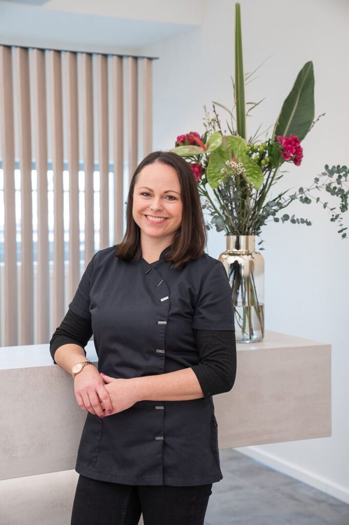 Claudia Behrmann, House Managerin, lächelt herzlich am Empfangstresen mit elegantem Blumengesteck im Hintergrund.