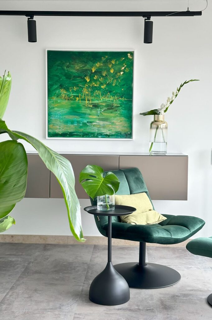 Grüner Lounge-Sessel mit Beistelltisch und Pflanze vor modernem Kunstbild im stilvollen Rooftop-Interieur.