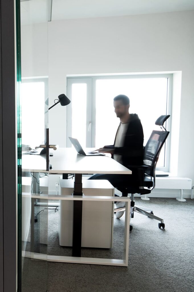 Mann arbeitet an höhenverstellbarem Schreibtisch mit Laptop in einem lichtdurchfluteten Büroraum im BUZZINLAB Stuttgart.